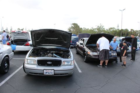 2003 Ford Crown Victoria - silver Ford sedan and a black Ford sedan sit with open hoods while a group of people gather to inspect them at a meet.