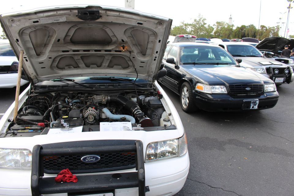 White Ford sedan with open hood beside black Ford sedan at car show