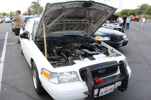 2003 Ford Crown Victoria - A white Ford Crown Victoria Police Interceptor with a black push bar sits hood-up at an outdoor car meet, the hood propped on a wooden stic…