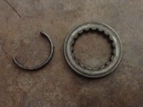 1986 Ford Bronco - Two metal automotive parts, a ring and a C-clip, are shown on a workbench.