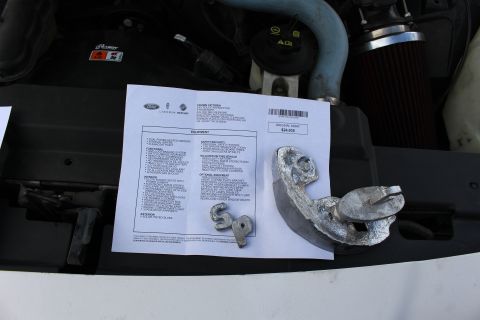 2003 Ford Crown Victoria - Lincoln-Mercury Crown Victoria window-sticker printout sits in an engine bay beside polished cast-metal letters and a part, with a red cone…