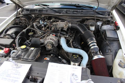 2003 Ford Crown Victoria - Detailed engine bay of a white full-size sedan showing a polished alternator, light-blue coolant hoses and a red cone air intake, with spec…