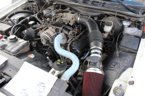 2003 Ford Crown Victoria - Close-up of a white sedan's V8 engine bay featuring a curved light-blue upper hose and a red conical air filter mounted on a black intake t…