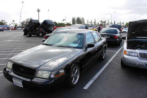 2003 Ford Crown Victoria - black Ford Crown Victoria sedan with aftermarket wheels parked at a car show, a silver car with open hood and a hot rod visible nearby.