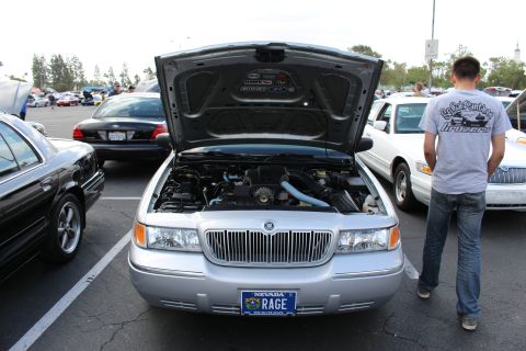 2003 Ford Crown Victoria - Front view of a silver Mercury Grand Marquis with its hood raised, wearing a Nevada vanity plate reading RAGE, a spectator standing at righ…