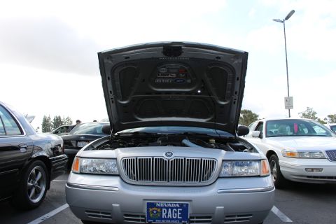 2003 Ford Crown Victoria - Head-on view of a silver Mercury sedan with its hood propped up, chrome grille and a Nevada plate reading RAGE visible at the front.