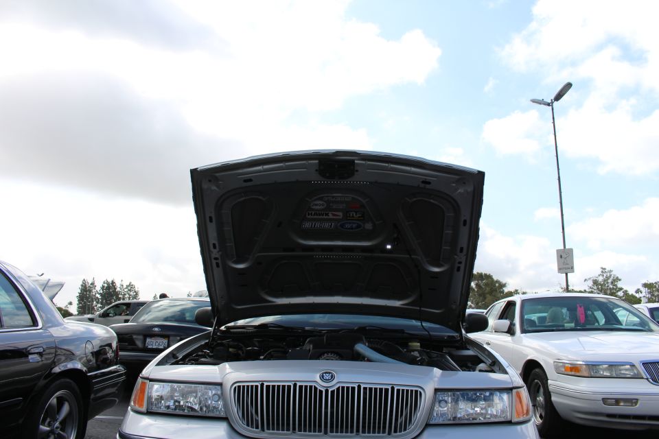 Underside of an open hood above a silver Mercury sedan against a cloudy sky