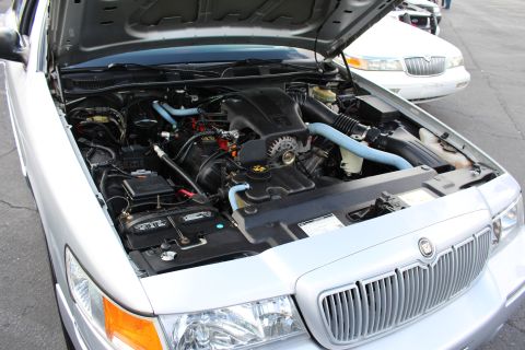 2003 Ford Crown Victoria - Detailed engine bay of a silver Mercury Grand Marquis showing a V8 with light-blue coolant hoses, with the chrome grille in the foreground.