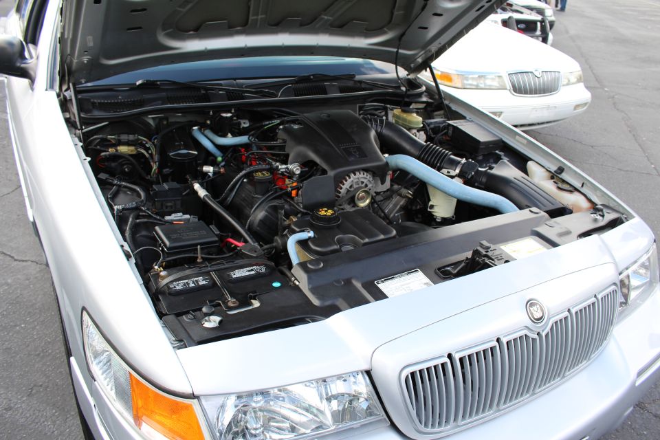 Engine bay of a silver Mercury Grand Marquis with blue hoses and V8 engine