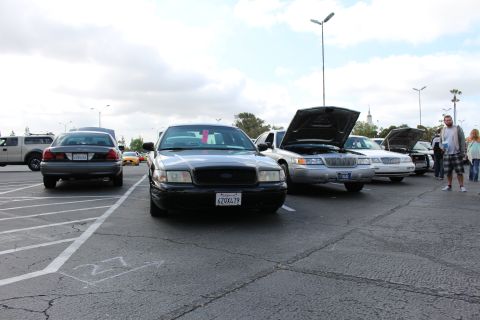 2003 Ford Crown Victoria - black Ford Crown Victoria faces the camera in a parking-lot car show, with a silver Mercury and other open-hood sedans lined up to the righ…