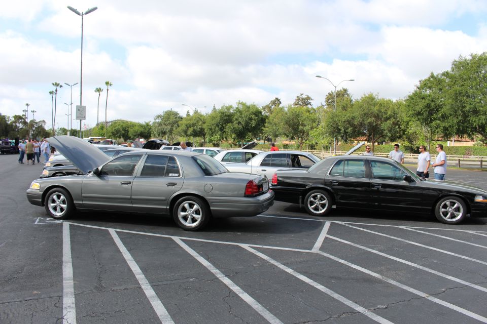 Grey sedan with open hood beside a black sedan at an outdoor car show