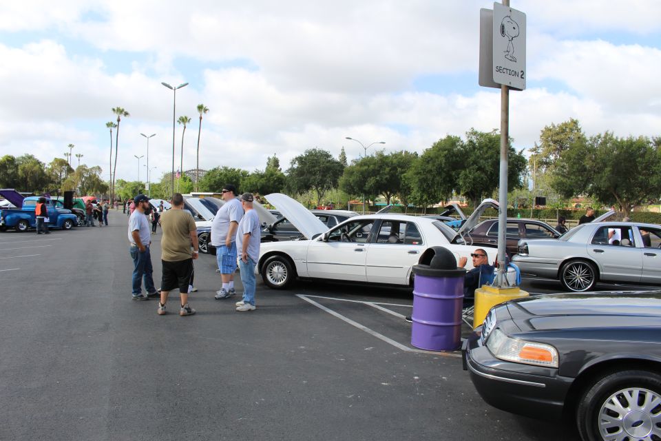 Car meet with white and gray sedans and people standing near a Snoopy sign
