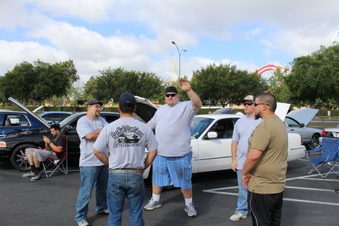 2003 Ford Crown Victoria - group of men stand and talk in front of a white full-size sedan with its hood open in a parking lot.