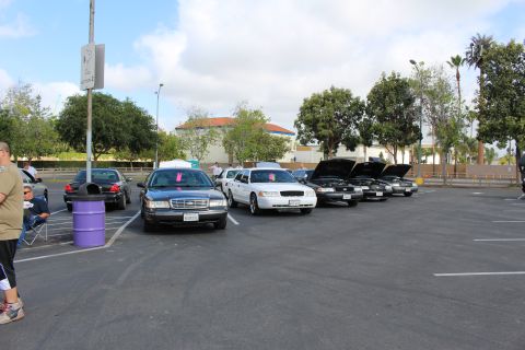 2003 Ford Crown Victoria - Black, gray and white full-size sedans are parked in a row, some with hoods up, in an open parking lot.