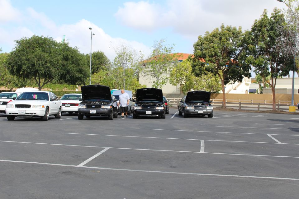 Three black Ford sedans with hoods open and a white sedan in a parking lot