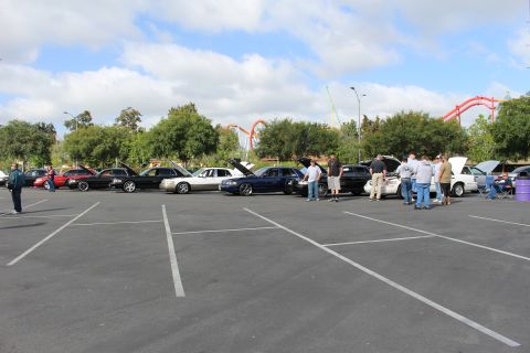 2003 Ford Crown Victoria - wide view of a parking-lot car meet shows rows of sedans with hoods open and people gathered, coasters in the background.