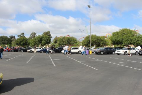 2003 Ford Crown Victoria - distant row of sedans and standing people fills one side of a large parking lot with roller coasters on the horizon.