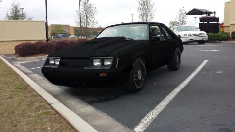 1994 Ford Bronco - A black coupe with a prominent hood scoop is parked in a lot, with a white sedan visible in the background.