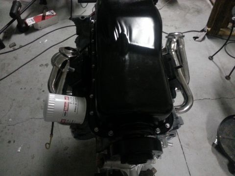 1994 Ford Bronco - Close-up of a Ford V8 engine, an oil filter and custom exhaust headers, on a workshop floor.