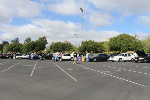 2003 Ford Crown Victoria - Distant sedans and people are scattered across a large parking lot with red roller coasters visible behind the trees.