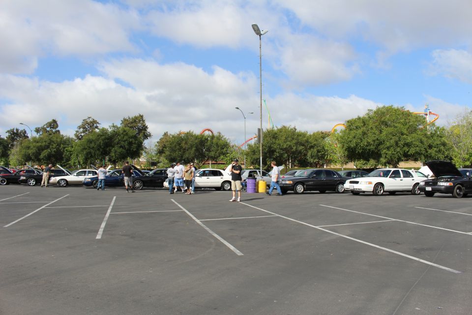 Distant cars and people in a large parking lot with roller coasters behind