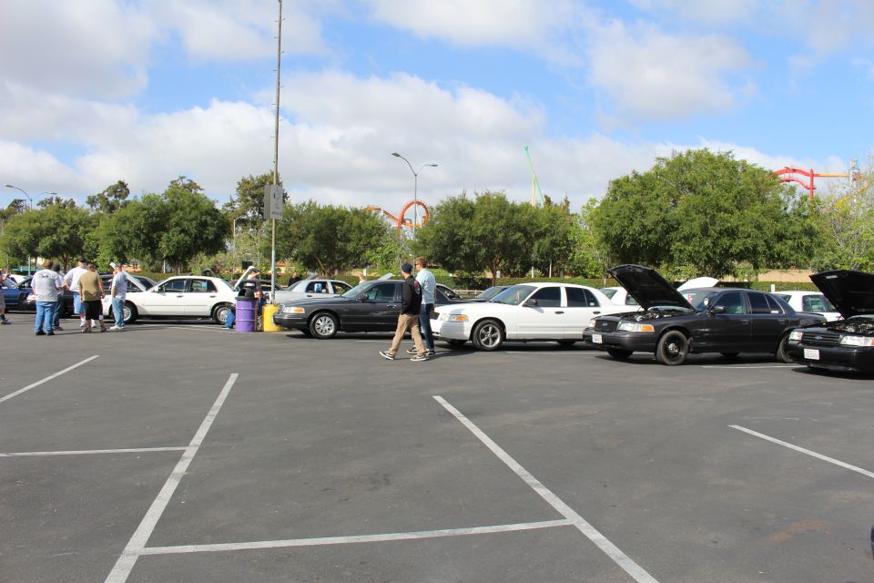 Row of full-size sedans with hoods open and people standing nearby in a parking lot