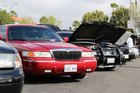 2003 Ford Crown Victoria - Close view of a red sedan marked EVIL MGM alongside black sedans with raised hoods and brush guards.