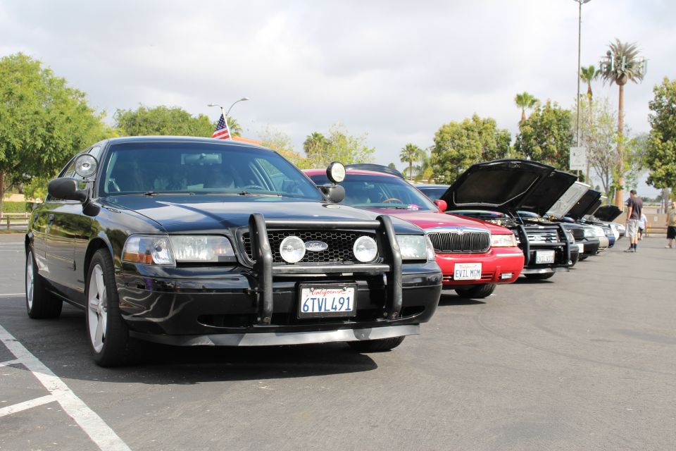 Black Ford sedan with push bar, plate 6TVL491, leading a row of cars and a flag