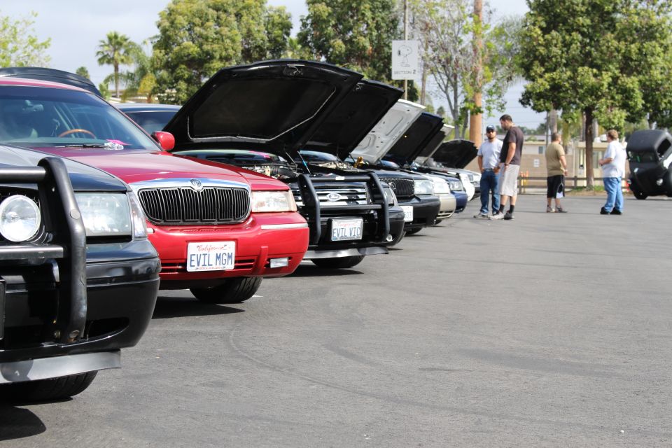 Lineup of sedans with raised hoods, red EVIL MGM car at center, people looking on
