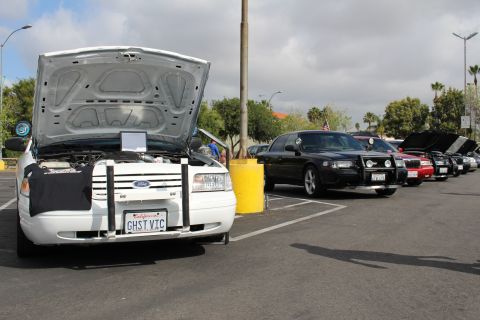 2003 Ford Crown Victoria - white Ford sedan with its trunk propped open and a GHST VIC plate leads a row of dark cars under a cloudy sky.