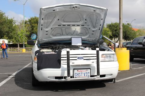 2003 Ford Crown Victoria - white Ford sedan displays its open trunk and a GHST VIC license plate, parked beside trees on an overcast day.