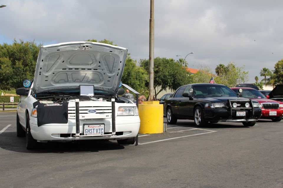 White Ford sedan with open trunk and GHST VIC plate next to a black sedan in a lot