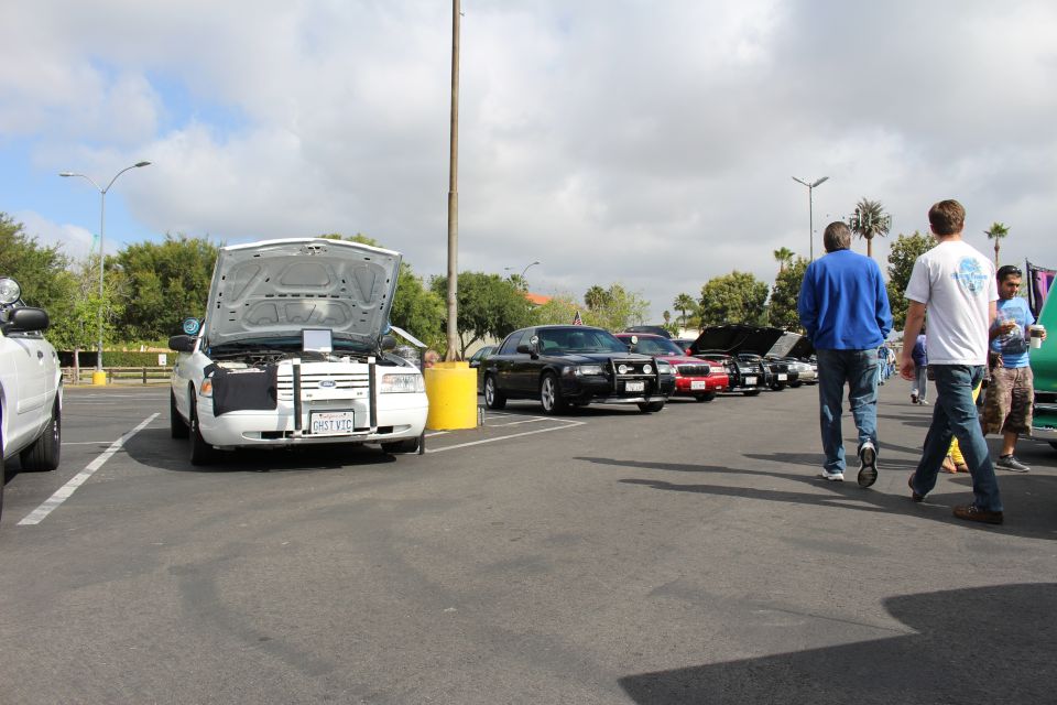 Wide view of a parking-lot car row with white Ford GHST VIC and people walking