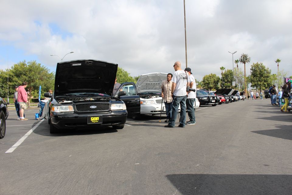 Black Ford sedan with open hood and two men talking in a parking-lot car meet
