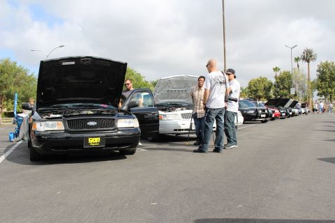 2003 Ford Crown Victoria - black Ford sedan shows its open hood while three men stand nearby along a row of cars in the lot.
