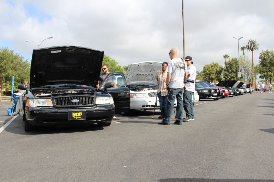 Black Ford sedan with raised hood and three men standing in a parking-lot meet
