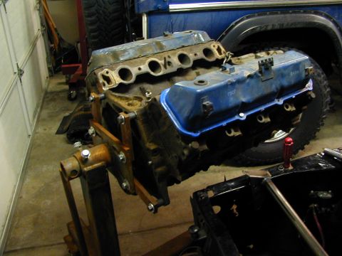 1979 Ford Bronco - Engine on a stand, with a blue vehicle's tire and fender visible in the background.