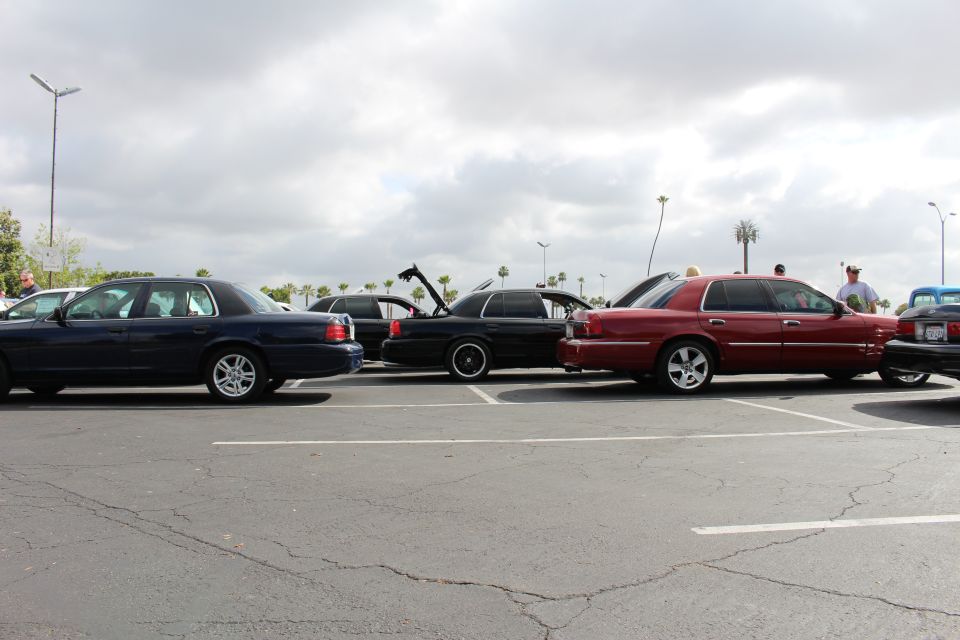Dark and dark-red sedans parked in a row in a lot with people nearby