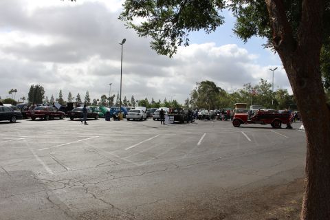 2003 Ford Crown Victoria - wide view of a car show in a large parking lot, with a vintage red truck visible at right and rows of cars in the distance.