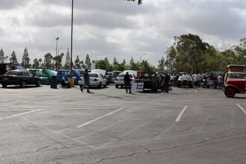 2003 Ford Crown Victoria - People and vehicles gather across a large parking lot at a car show, with a vintage open-bodied car parked at right.