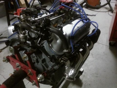 1994 Ford Bronco - Engine on a red stand, with blue spark plug wires and chrome exhaust headers.