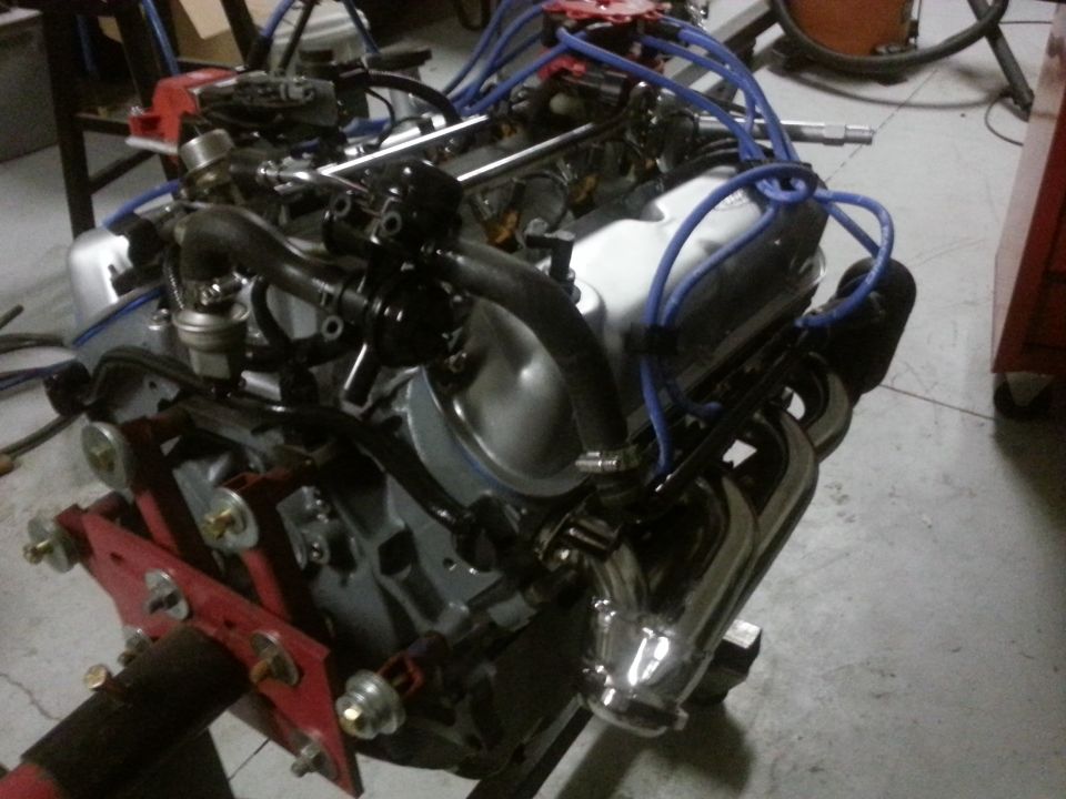 Engine on a red stand, with blue spark plug wires and chrome exhaust headers