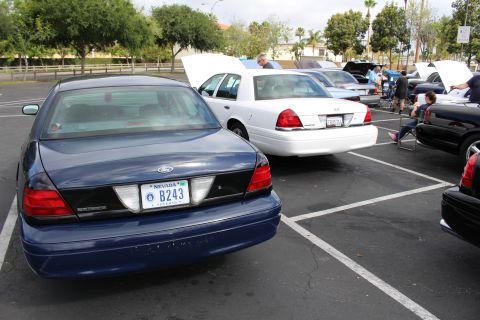 2003 Ford Crown Victoria - rear of a dark blue Ford sedan showing a Nevada plate reading B243, with a white sedan and people behind it.