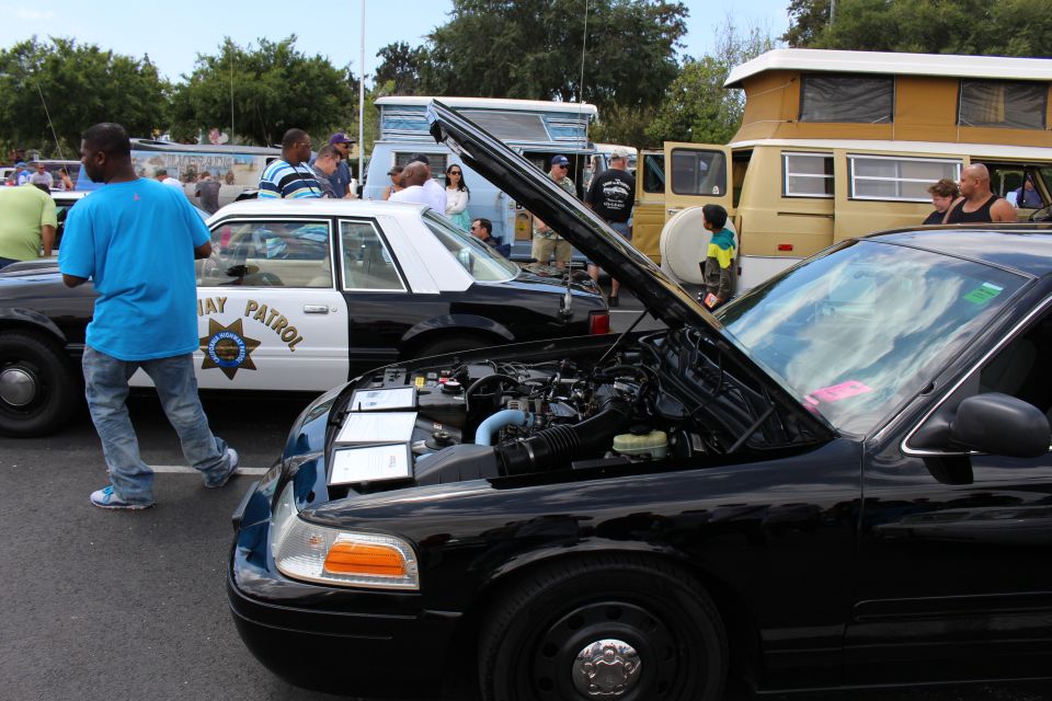 Black sedan with open hood beside Highway Patrol car at show