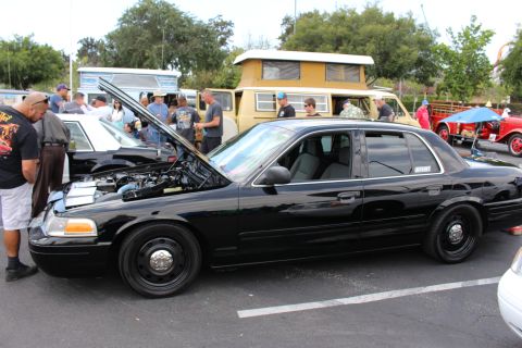2003 Ford Crown Victoria - black Ford sedan with its hood up and black steel wheels sits at a car show as people browse nearby.