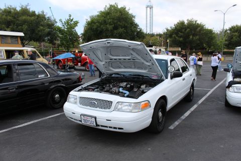 2003 Ford Crown Victoria - white Ford Crown Victoria sedan sits with its hood up at a sunny outdoor parking-lot car meet.