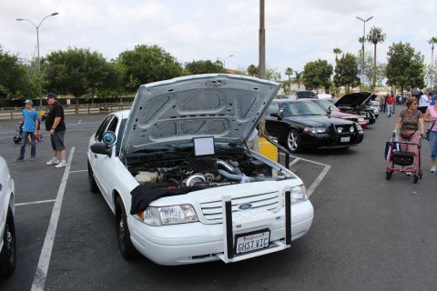 2003 Ford Crown Victoria - front of a white Ford sedan shows an open hood and modified engine bay at a parking-lot car show.