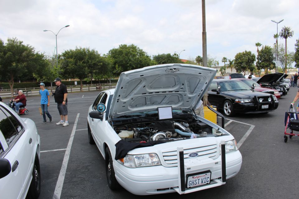 White Ford sedan with hood up next to black sedans in show parking lot