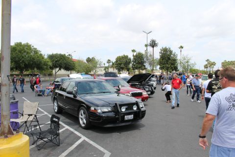 2003 Ford Crown Victoria - black sedan fitted with a front brush guard sits among parked cars and spectators at an outdoor meet.