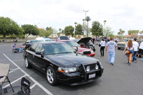 2003 Ford Crown Victoria - black sedan with a front brush guard and gray alloy wheels is parked at a busy parking-lot car show.